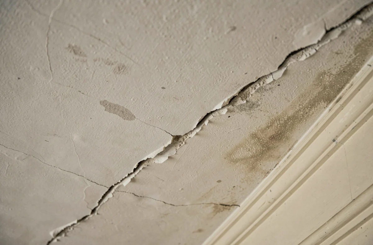 Gros plan d'une fissure diagonale sur un plafond en plâtre ancien d'un appartement à vendre nécessitant une réparation
